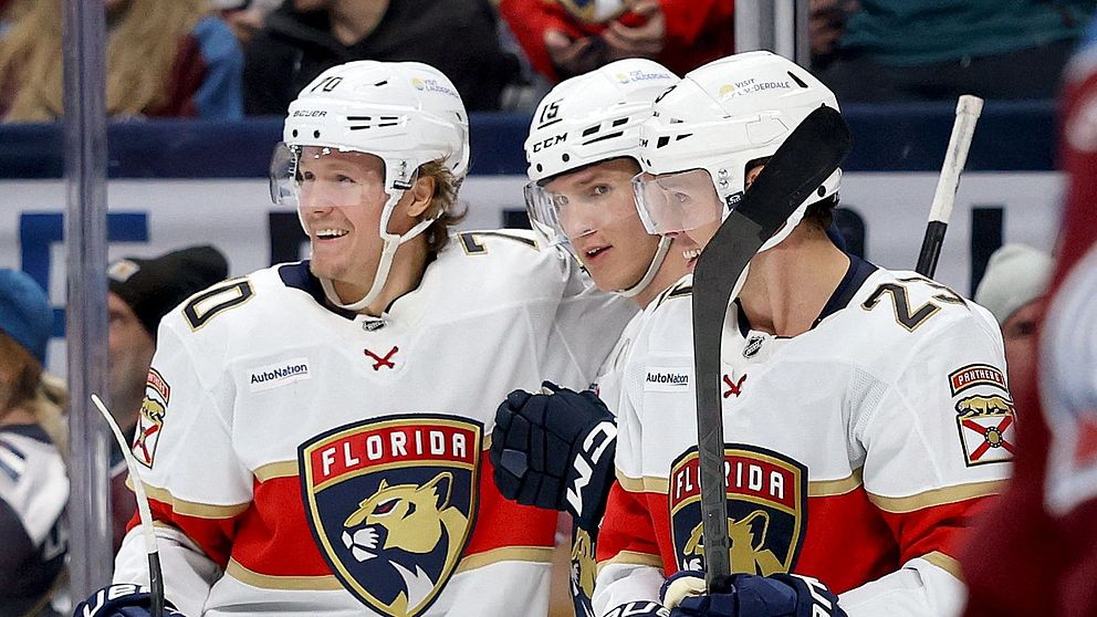 Spelare från Florida Panthers firar ett mål under en hockeymatch, medan en motståndare från Colorado Avalanche står i bakgrunden, tydligt besviken. Åskådare i publiken är klädda i lagets färger och visar engagemang för matchen.