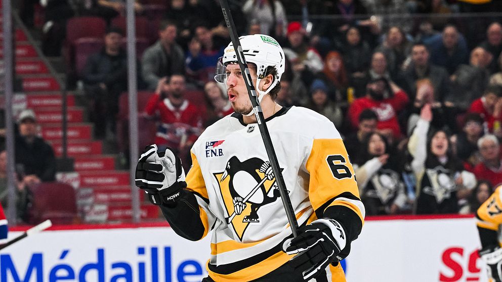 En hockeyspelare i en gul och svart tröja med nummer 6, tillhörande Pittsburgh Penguins, gestikulerar och firar en prestation under en match. Publiken i bakgrunden är engagerad och flera åskådare syns på läktaren.