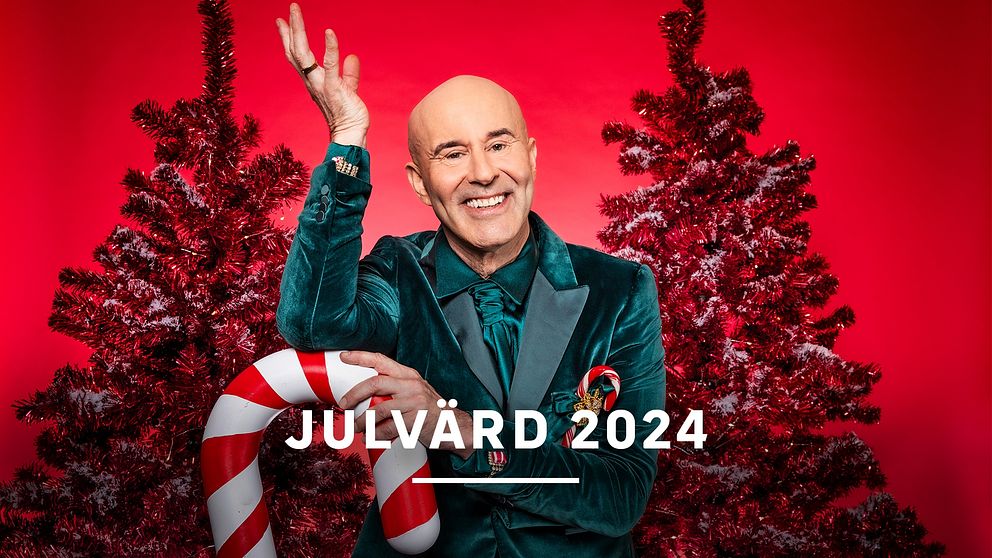 En festligt klädd person som håller i en godiskäpp framför två julgranar, med en röd bakgrund, och texten ”JULVÄRD 2024” i mitten.