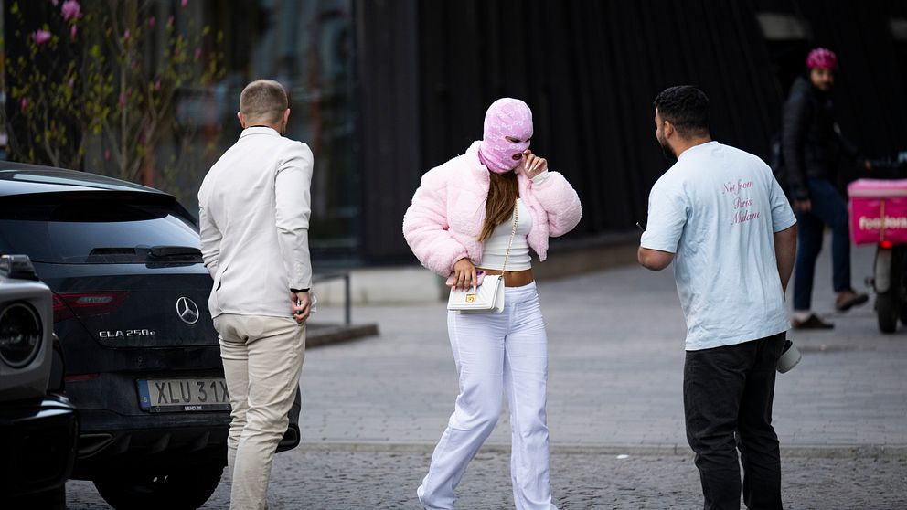 ”Nya” Fröken Snusk i rosa mask och vit outfit utomhus med två män