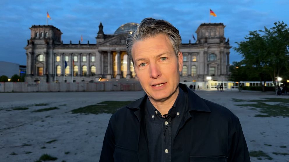 Person står framför riksdagshuset i Berlin under kvällstid.