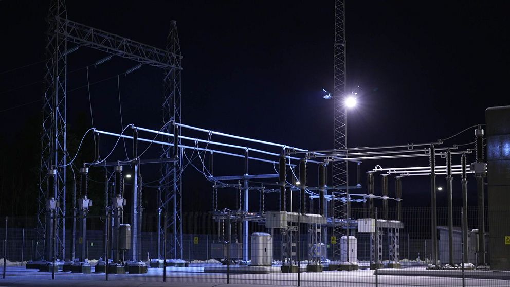 Nattbild av en transformatorstation med belysning som lyser upp ledningar och utrustning, omgiven av stängsel.