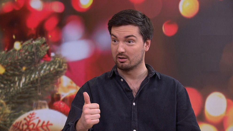 En person visar ett tummen upp-gester och är klädd i en mörk skjorta, i en miljö med juldekorationer och suddiga ljus som skapar en festlig atmosfär.