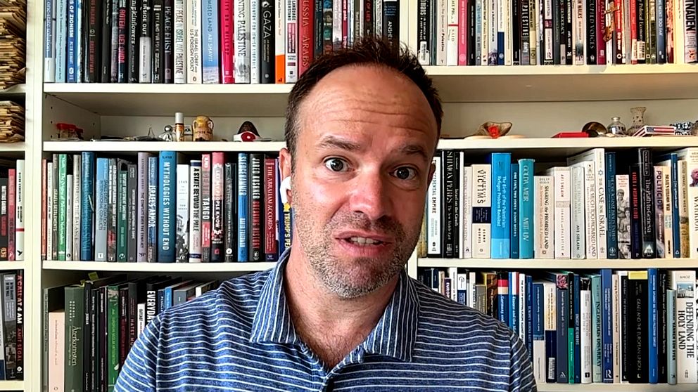 Anders Persson framför bokhylla kommenterar avtalet om att Gaza ska avväpnas