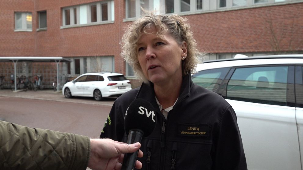 En person utanför ett flerfamiljshus intervjuas av någon från SVT med en mikrofon. Personen bär en svart jacka med märkning ”Västanfors Västervåla” och står framför en parkerad bil.