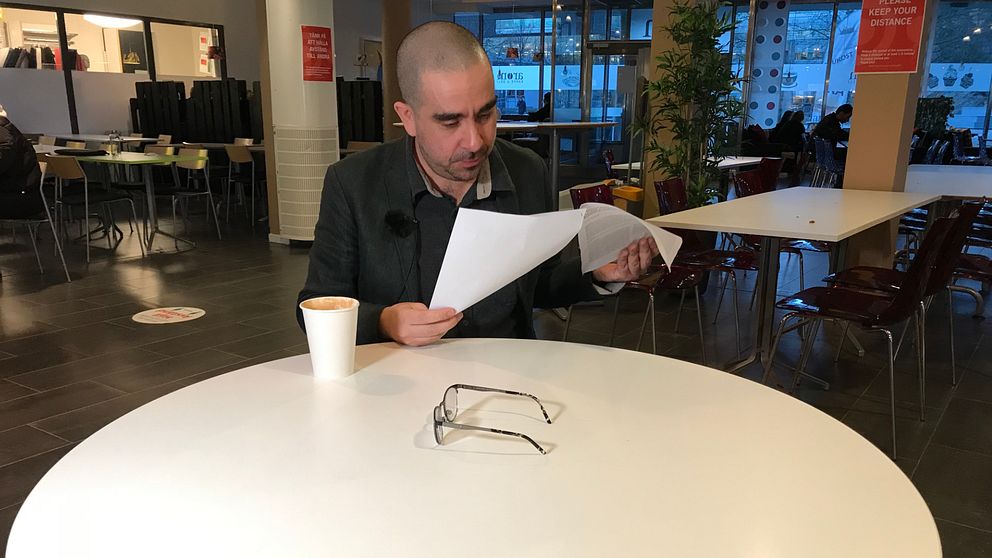 Person läser dokument vid cafébord; glasögon och kaffemugg på bordet.