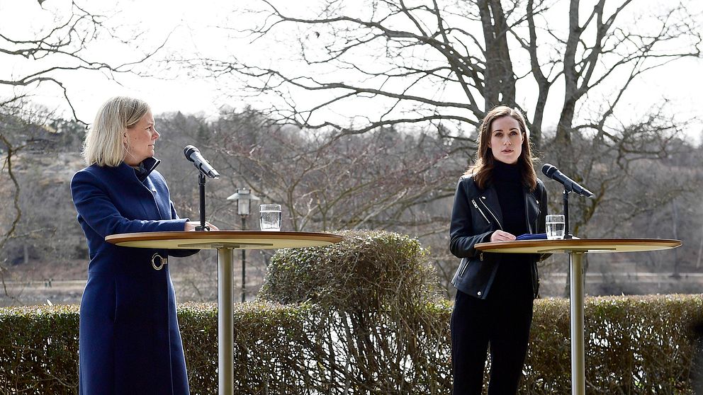 Två kvinnor talar vid ståbord utomhus, mikrofoner framför dem.
