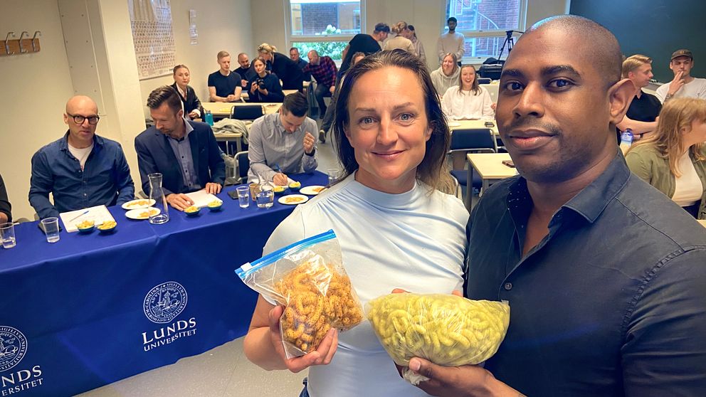Anna Jönsson och David Lundgren poserar, framför juryn i ostbågetävlingen, med varsin påse ostbågar i händerna.