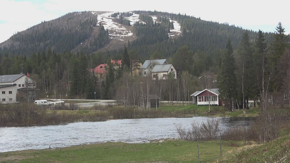 sjö i förgrunden, några hus och en fjälltopp