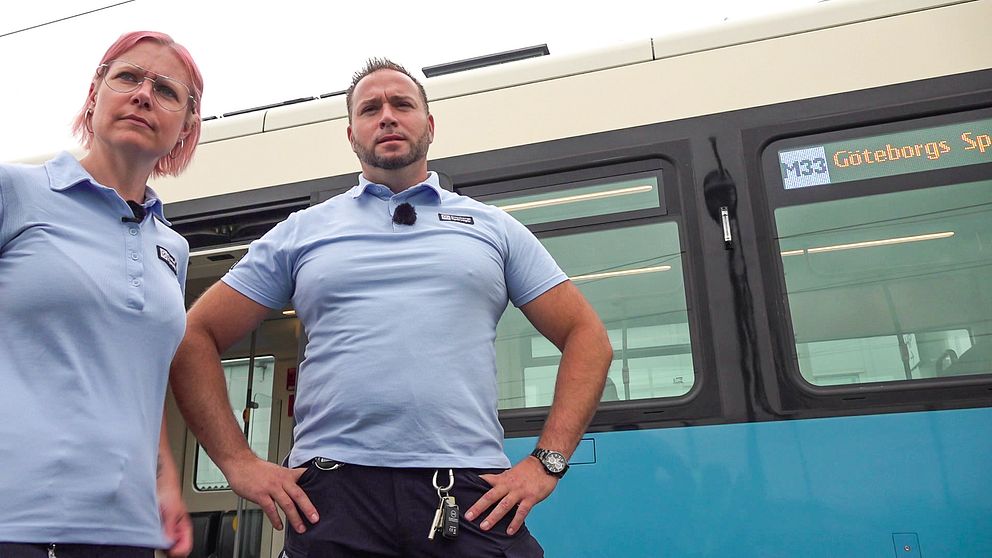 Två personer i spårvagnsföraruniform som står framför en spårvagn. De ser allvarliga ut.