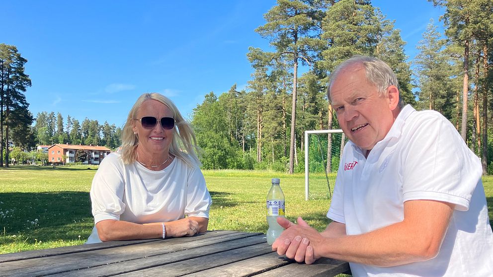 En man och en kvinna sitter på varsin sida av en parkbänk och tittar in mot kameran med ett leende. Båda har ett vitt plagg på överkroppen.