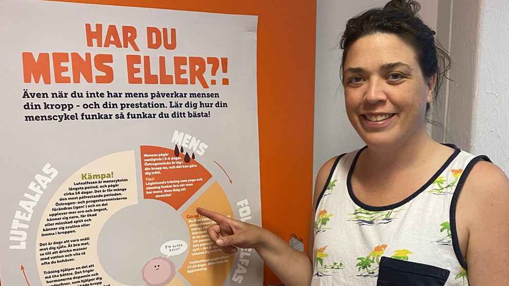 Louise Berg framför en affisch på en vägg.