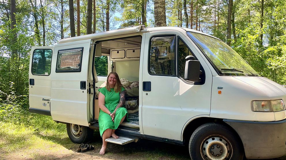 Marie sitter vid ingången till sin skåpbil som är parkerad i skogen. Hon ler mot kameran.