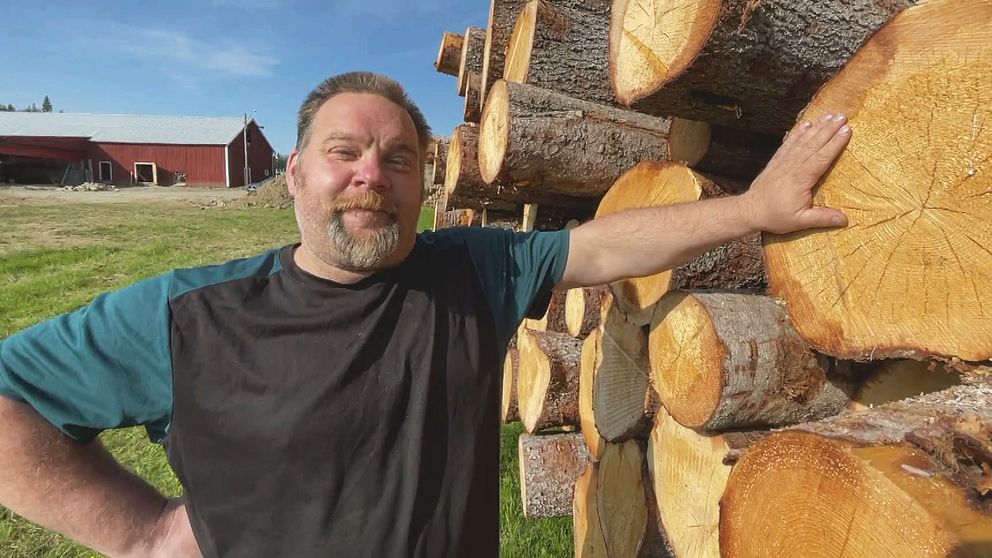 Tomas Granström, en man i medelåldern med kort hår, står vid ett timmerlass och ler.