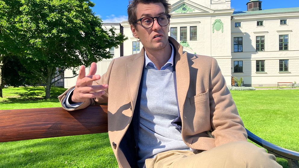 Gustav Krantz, en ung man i glasögon, sitter på en bänk i en park.