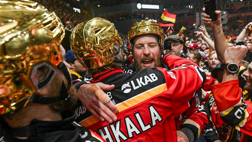Hockeyspelare firar seger på isen omgivna av publik, flera bär guldhjälmar.