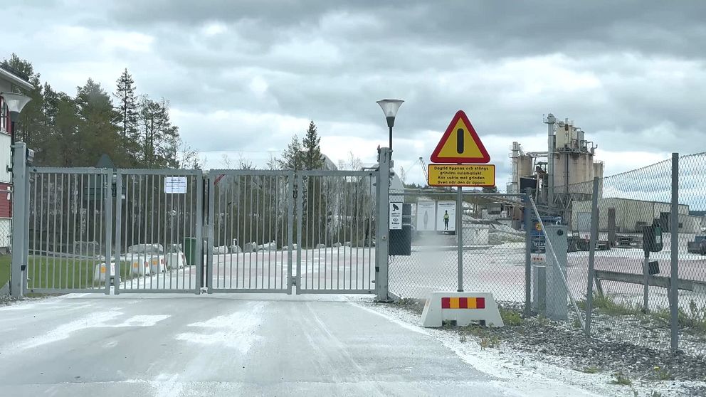 Industrigrind med varningsskylt och grå molnig himmel i bakgrunden.