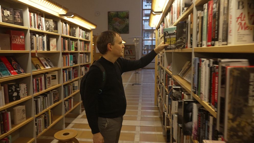 En person står vid en bokhylla i ett bibliotek och sträcker sig efter en bok.