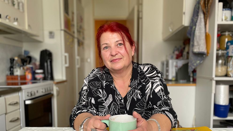 Viktoria sitter vid köksbordet och håller i en kaffemugg.