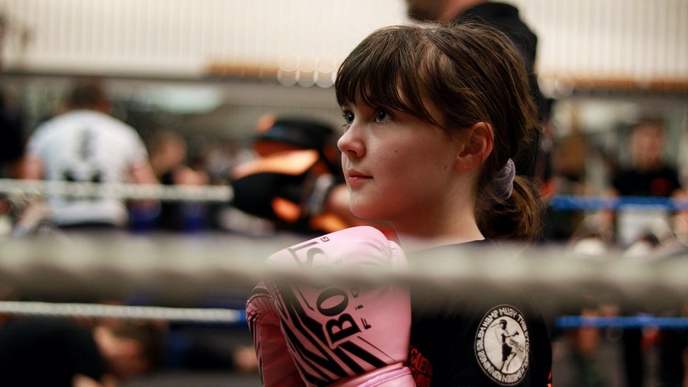 En tjej har på sig rosa boxningshandskar och står i en boxningsring.