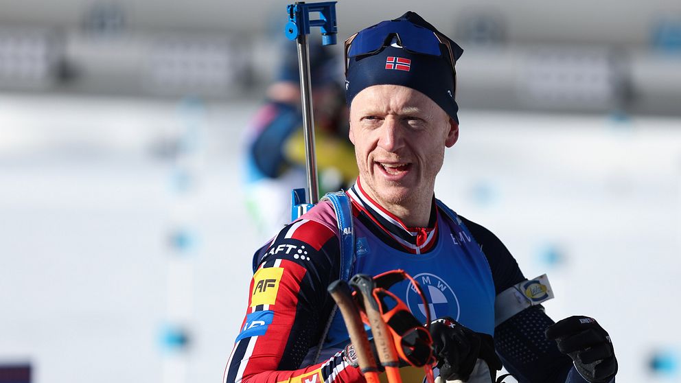 En skidskytt i tävlingsdräkt håller sina stavar medan ett gevär är fäst på ryggen under en biathlon-tävling.