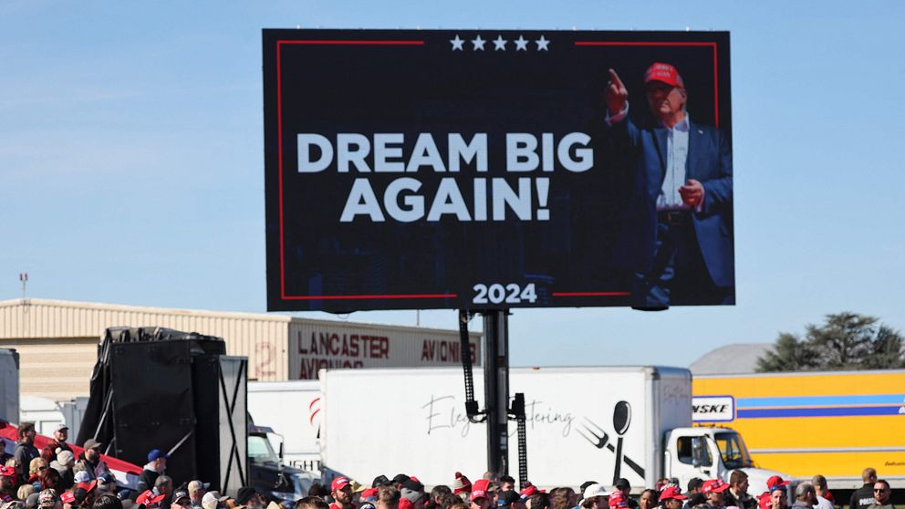 En stor digital reklamskylt visar texten ”DREAM BIG AGAIN!” och en bild på Donald Trump.