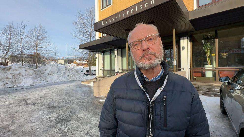 En person står framför ett Länsstyrelsen-kontor i ett vinterlandskap med snö på marken och träd i bakgrunden.