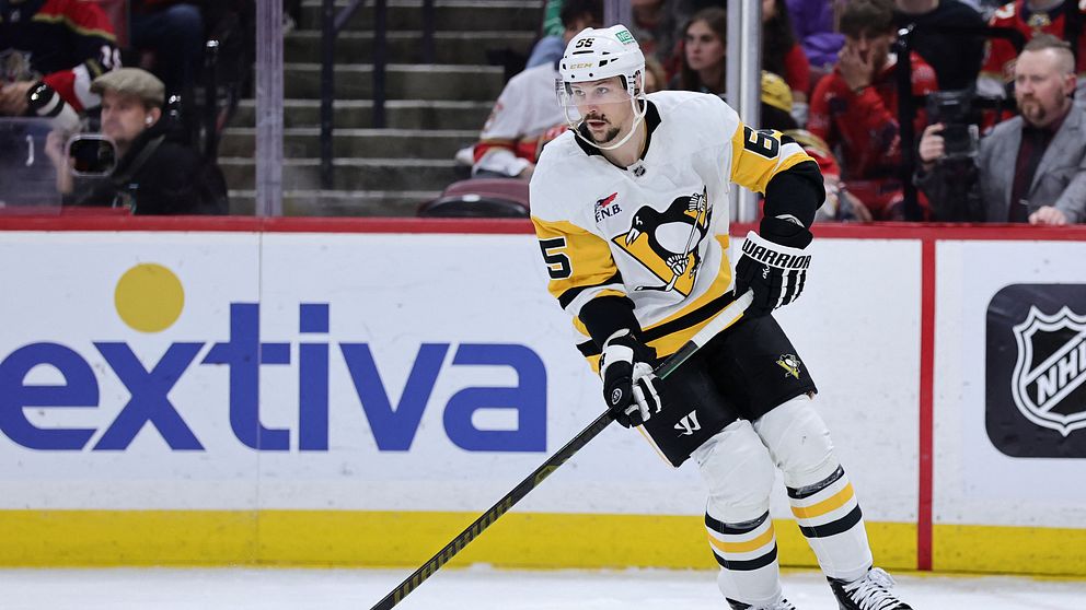 Hockeyspelare i Pittsburgh Penguins tröja skjuter pucken på isen under en match. I bakgrunden syns entusiaster i publiken.