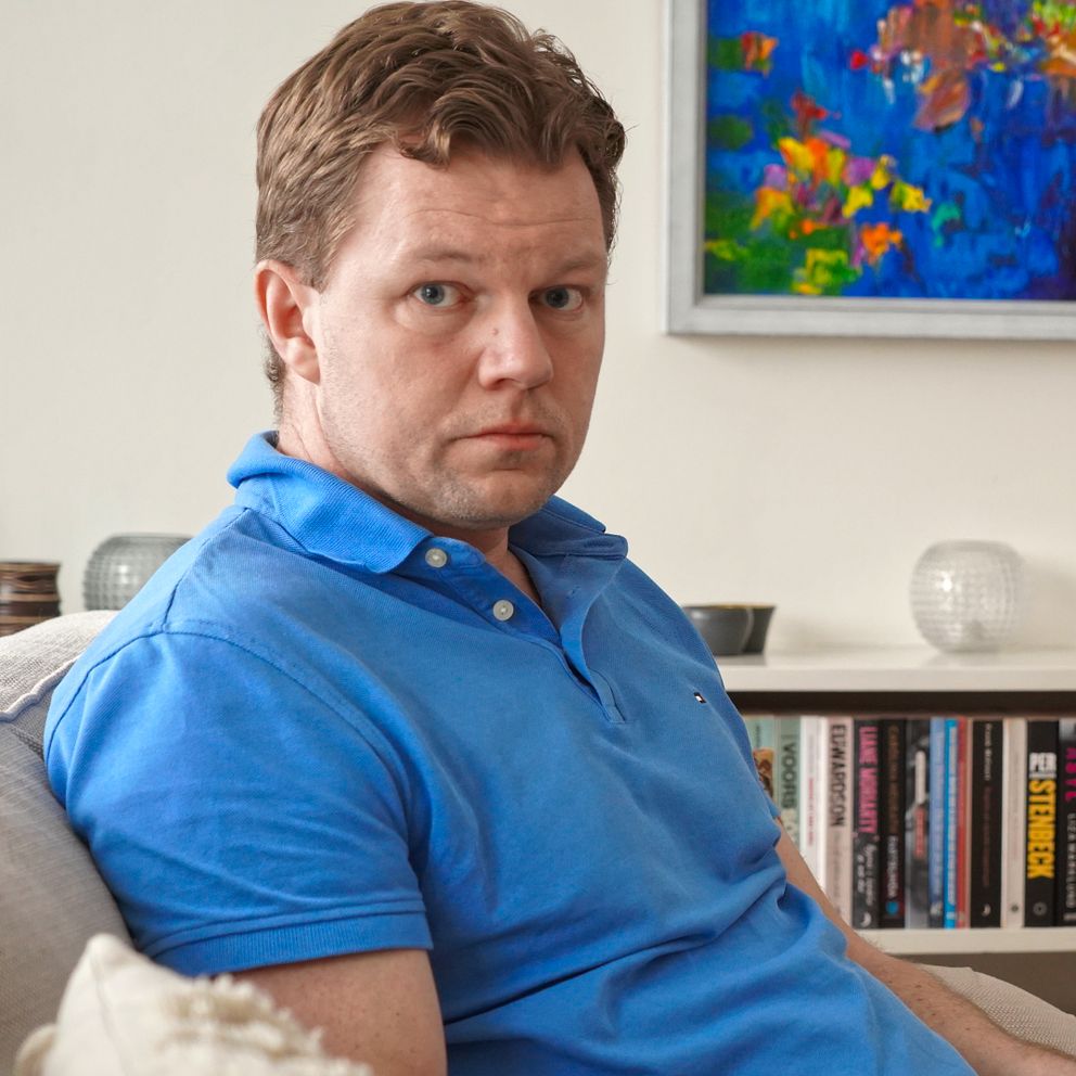 Man i blå tröja tittar med fotografi i handen.