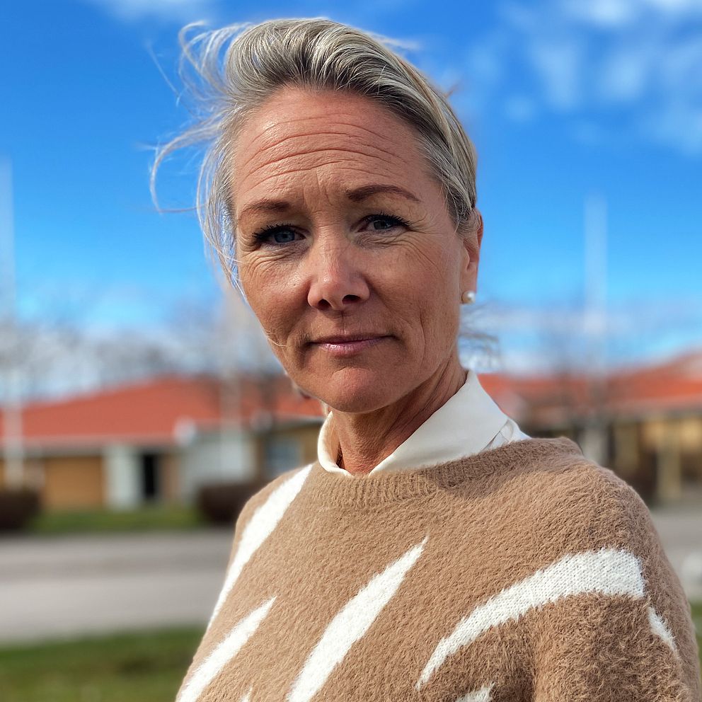 Person vid väg med röda hus och blå himmel i bakgrunden.