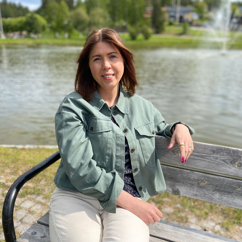 Hanna Öhman sitter på en bänk utomhus och till höger syns händer som bildar ett hjärta på en gravidmage.
