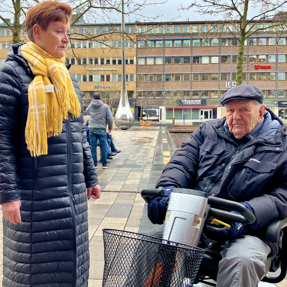 En man i permobil och en kvinna som står och har gul halsduk på sig.