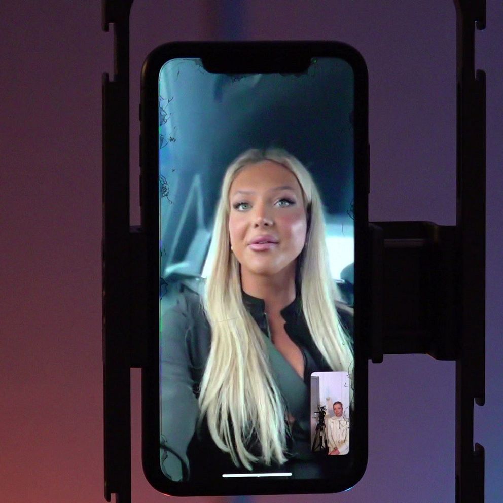 En mobiltelefon som visar en videochatt. Skärmen visar en person med långt hår i en bil. Till höger syns en annan bild av en kvinna och ett barn som sitter nära varandra.