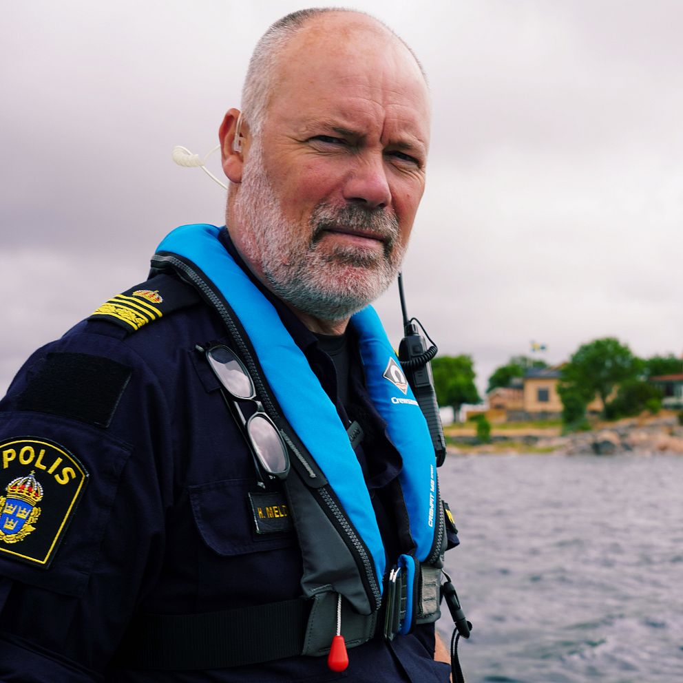 Båtpolis står på en båt med skärgården i bakgrunden.