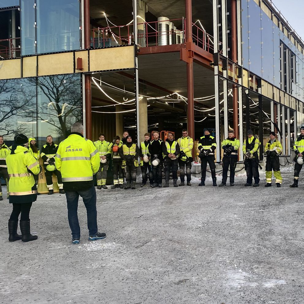 På bilden syns flera personer som är iklädda varselkläder på ett bygge i Härnösand. De har tagit av sina hjälmar och håller en tyst minut efter hissolyckan i Sundbyberg förra veckan.