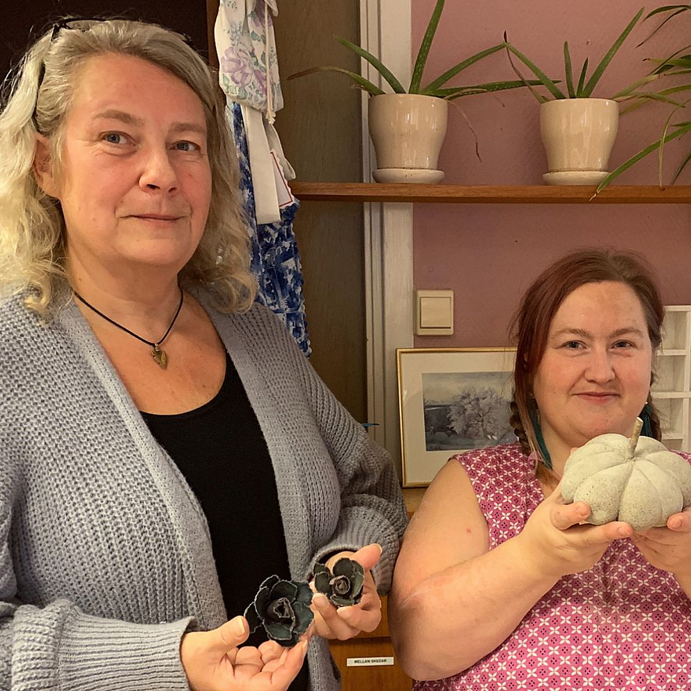 Arbetshandledaren Tina Carlström och deltagaren Therese Andersson håller upp några av deltagarnas hantverk – några stearinrosor och en betongpumpa.
