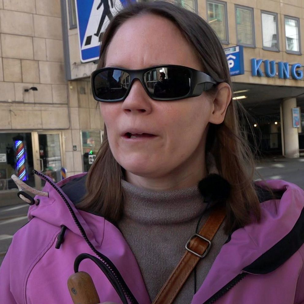 Person i rosa jacka framför garage. En bil och byggnad syns i bakgrunden.