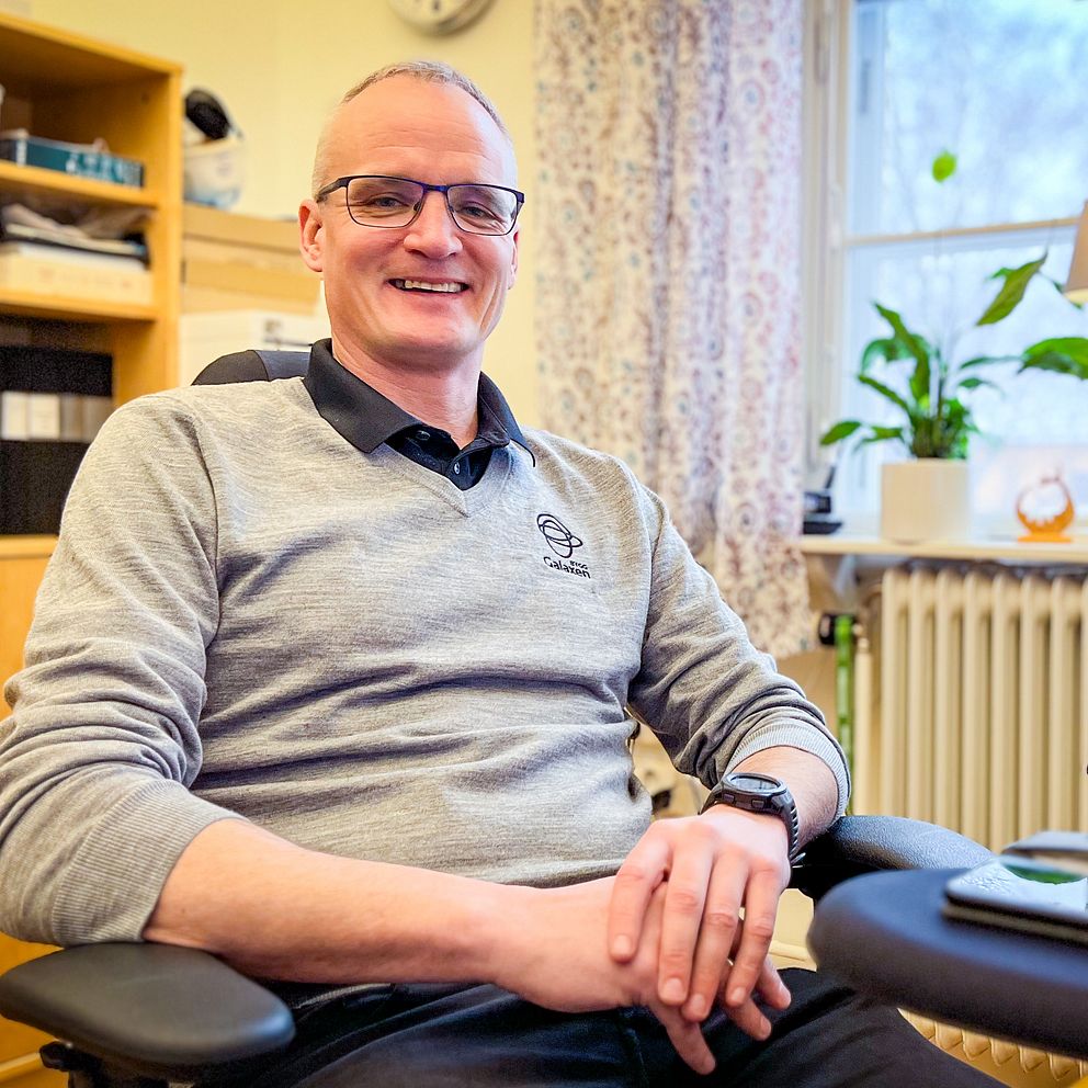 En glad man i grå tröja sitter vid sitt skrivbord