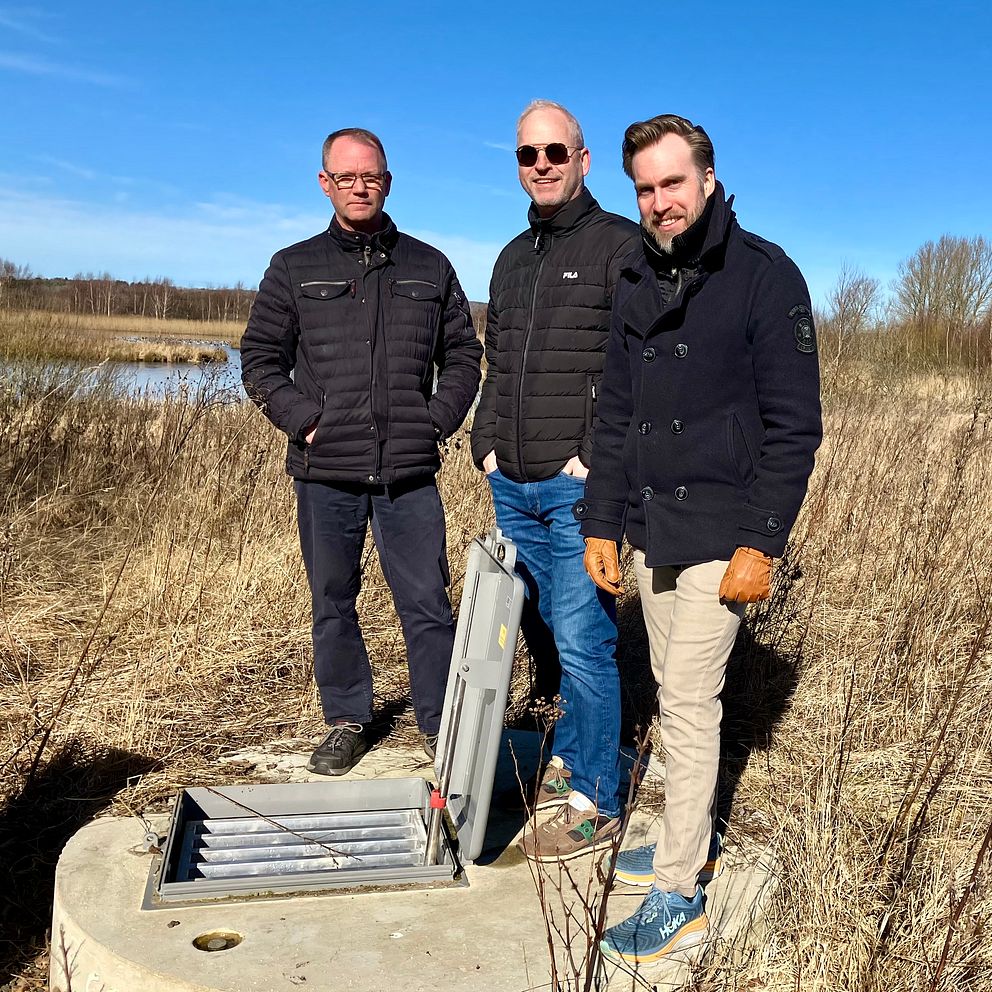 tre män vid ett brunsslock