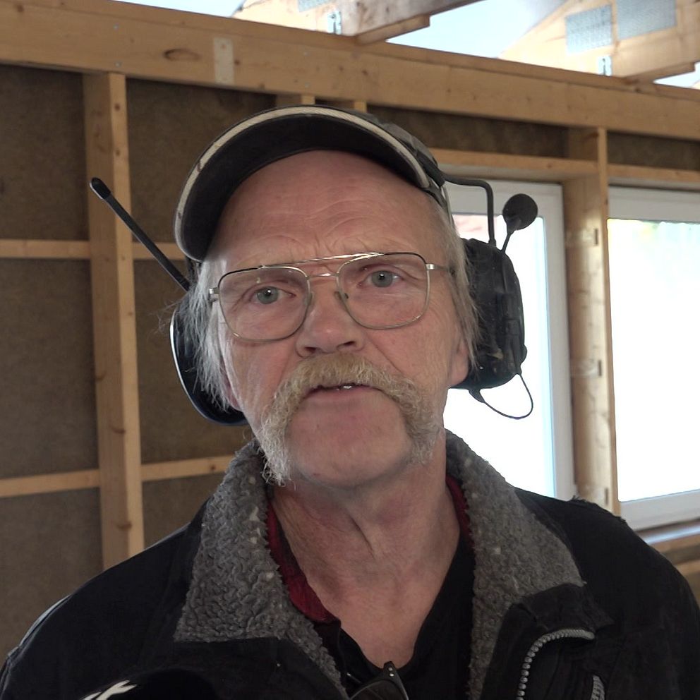 Peder Näslund står inne i nybygget, han har mustasch och glasögon och har på sig en keps och hörselkåpor.