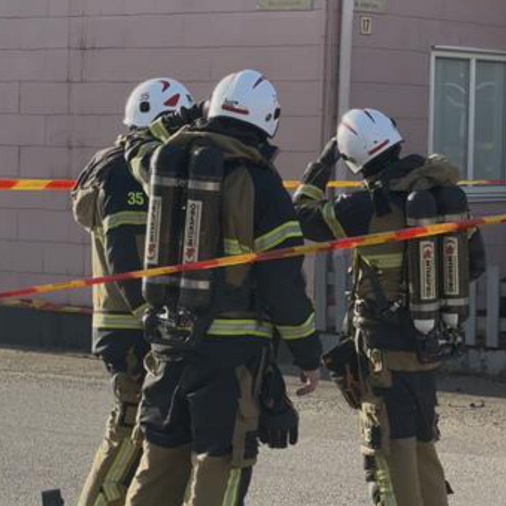 Brandmän i skyddsutrustning står vid avspärrning framför ett rosa hus.