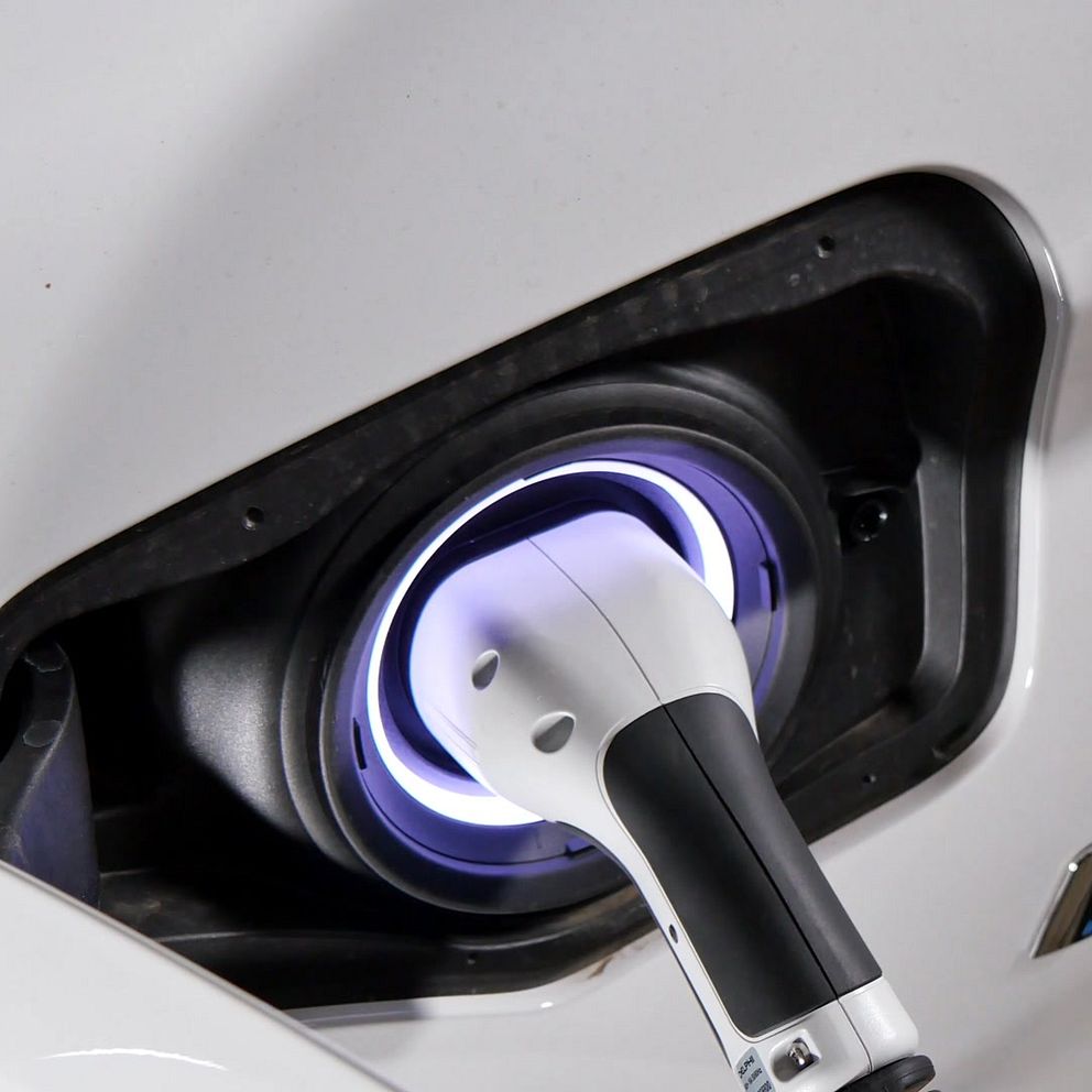 ALT-text: En närbild av en laddningssladd som är ansluten till laddningsporten på en hybridbil, med en lila belysning runt porten som indikerar att bilen laddas. Bakgrunden är suddig och fokuserar på kopplingen.