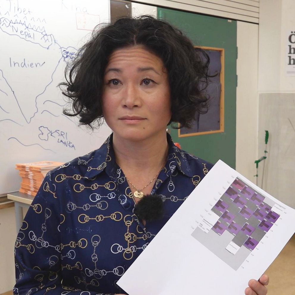 På Bilden syns Helen Nilsson, fackordförande för lärarfacket i Halmstad. Hon håller upp ett schema framför sig. Hon står i ett klassrum och i bakgrunden syns en whiteboardtavla.