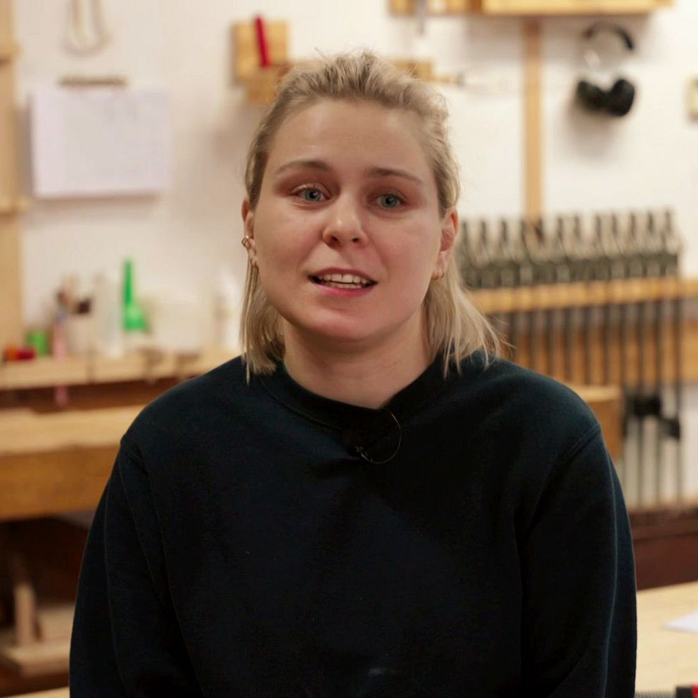tjej i mörk tröja sitter i en snickarverkstad med verktyg på väggen i bakgrunden