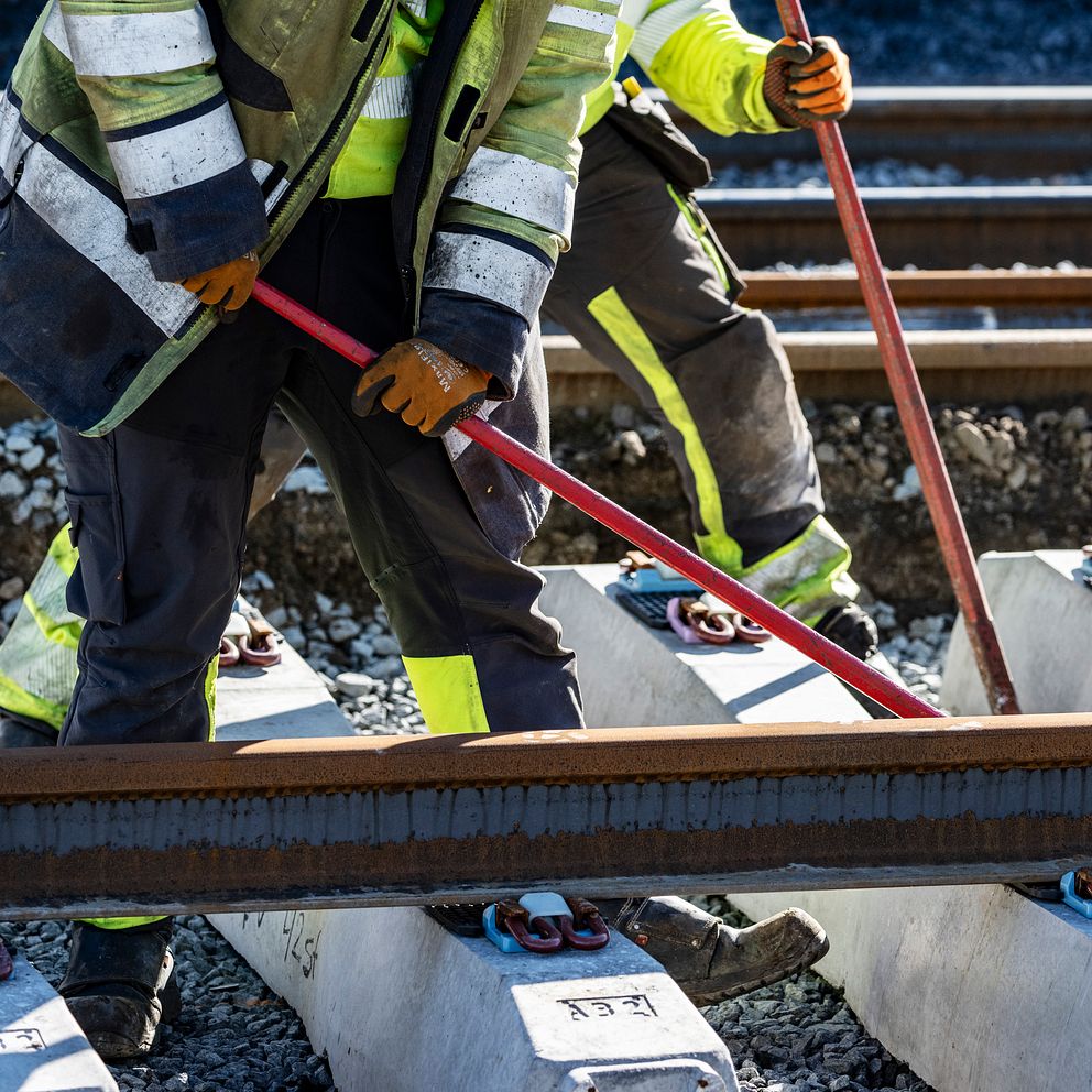 Bild på en järnväg och två personer iklädda varselställ som arbetar på spåret..