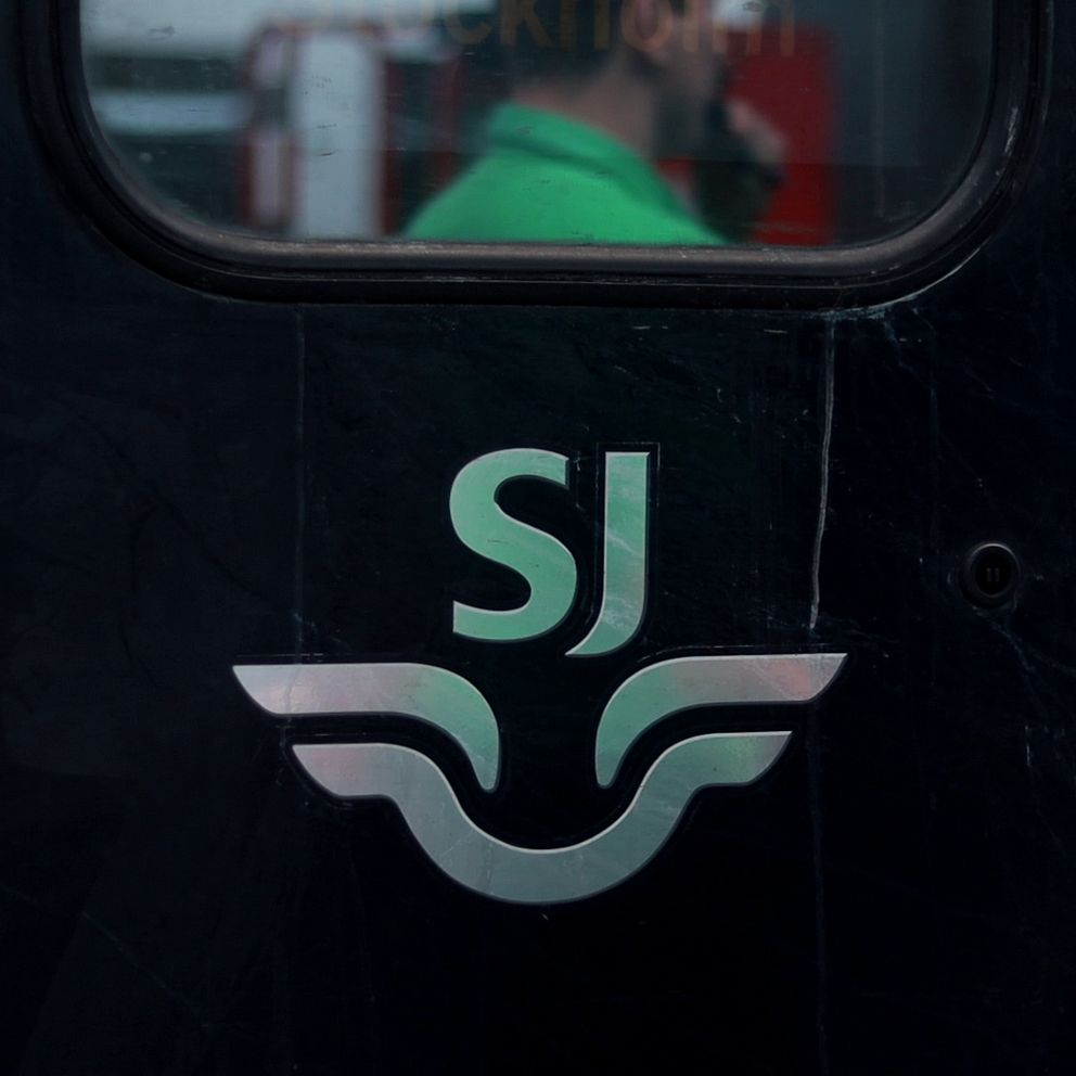 Tågvärd blåser i visselpipa framför logga med SJ