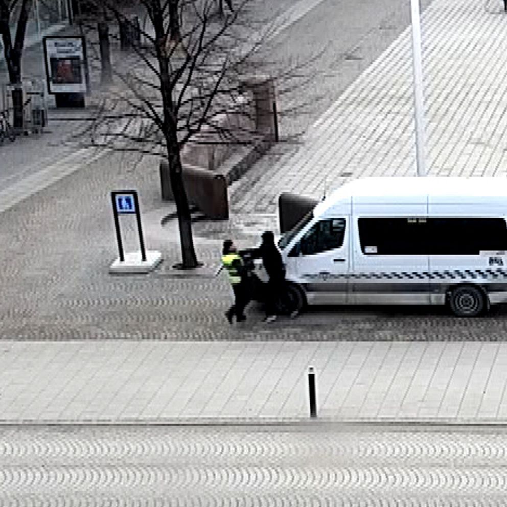 Två personer knuffas nära en vit skåpbil på en tom gata i stadsmiljö.