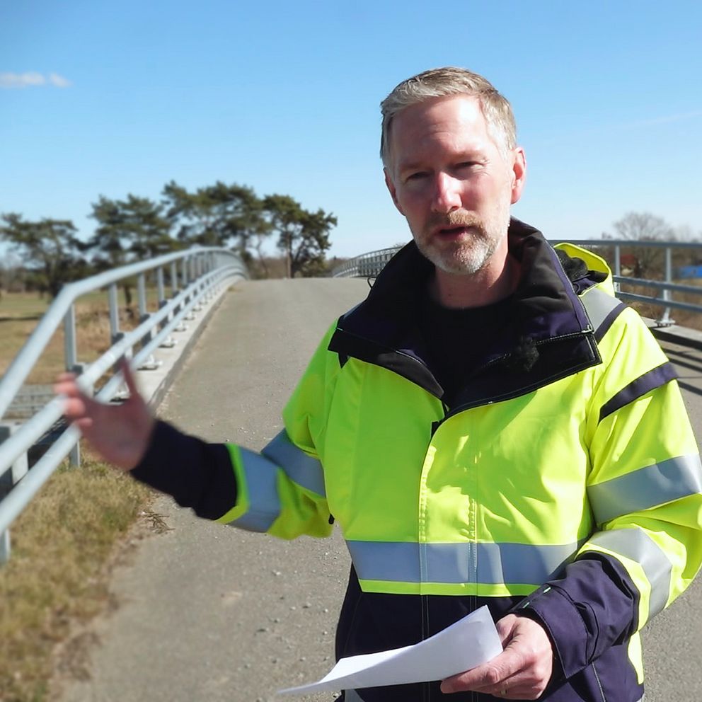 Jimmie Östling, projektledare på Trafikverket, står i gul arbetsjacka på en vägbro och håller ett papper.