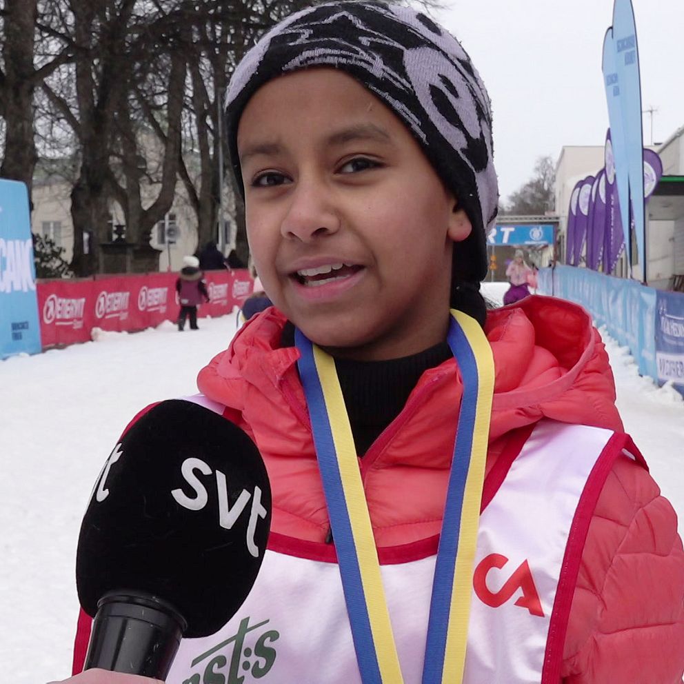 En person klädd i skidåkarkläder intervjuas av en SVT-reporter vid ett vinterevenemang med snöiga omgivningar och reklam för Skidklassikern.se i bakgrunden.