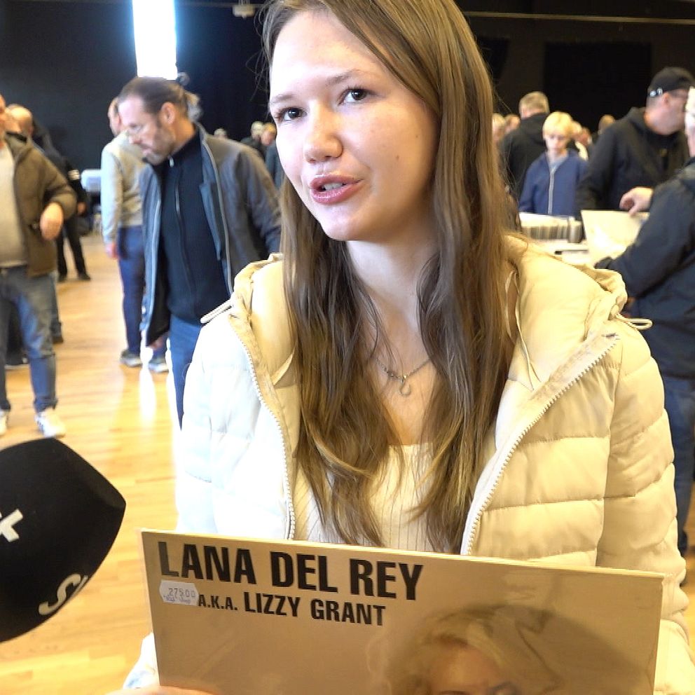 Ung kvinna som håller en vinylskiva med albumet ”Lana Del Rey” i en stor lokal med många människor. Det pågår en skivmässa där besökare letar efter skivor och pratar med varandra. En mikrofon med SVT:s logotyp syns i bilden.